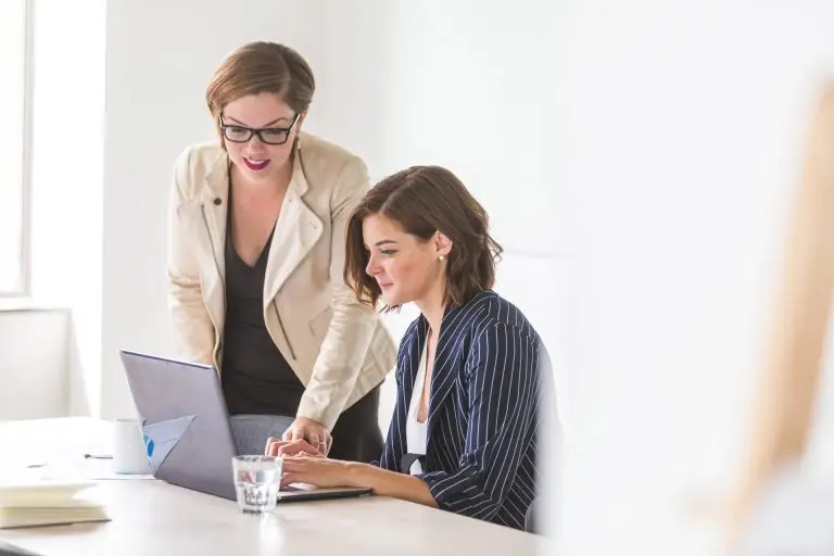 Two women sitting at a desk looking at a laptop