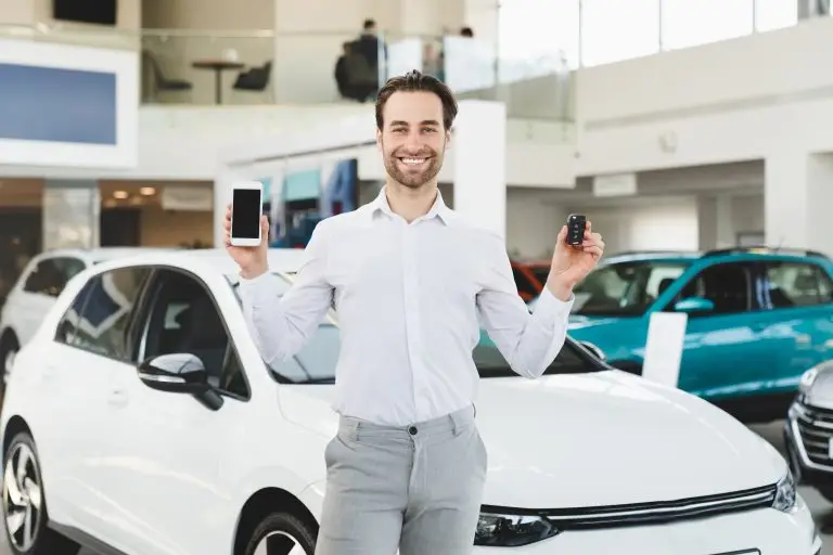 Man Car Dealer holding keys in front of a new car